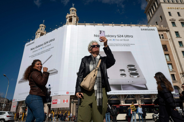 모바일월드콩그레스(MWC) 2024가 열리는 스페인 바르셀로나에 설치된 삼성전자 대형 광고판 앞에서 한 여성이 스마트폰으로 사진을 촬영하고 있다. 바르셀로나=AFP연합뉴스