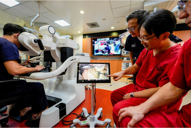 일본 후지타보건대(FHU) 외과의사들이 싱가포르국립대병원(NUH) 의사들과 함께 싱가포르 현지에서 원격조종장치로 일본 가고야에 있는 로봇팔을 움직여 위 절제 수술을 시연하고 있다. 사진 가운데에 위치한 작은 모니터를 통해 일본에서 원격으로 진행되는 수술 장면이 중계되고 있다 사진 제공=NUH