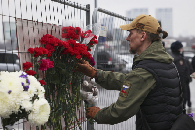 무차별 테러 공격으로 200여 명의 사상자가 발생한 러시아 모스크바 ‘크로커스 시티홀’ 공연장 인근 펜스에 한 주민이 꽃다발을 높고 있다. AP연합뉴스