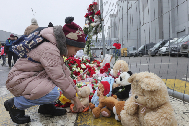 한 러시아 아이가 23일 테러 및 방화로 다수의 피해가 발생한 모스크바 ‘크로커스 시티홀’ 공연장 인근 거리에 꽃을 두고 있다. AP연합뉴스