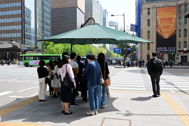 낮 최고기온이 내륙을 중심으로 25도 이상 올라 더운 날씨를 보인 18일 서울 세종대로사거리에서 대다수 시민들이 그늘막 안에서 보행 신호를 기다리고 있다.