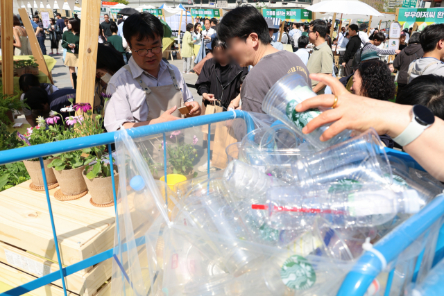 13일 서울 광화문광장에서 열린 ‘2024 지구의 날’ 기념행사에서 자원 순환 캠페인에 참여한 시민들이 일회용품을 주고 봄꽃을 받아가고 있다. 연합뉴스