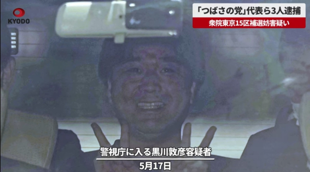 17일 타 진영의 선거 활동을 방해한 혐의로 경찰에 체포된 일본 정치 단체 ‘쓰바사의 당’ 대표 구로카와 아츠히코가 경시청으로 들어가는 차량 안에서 카메라를 향해 웃고 있다./교도통신 영상