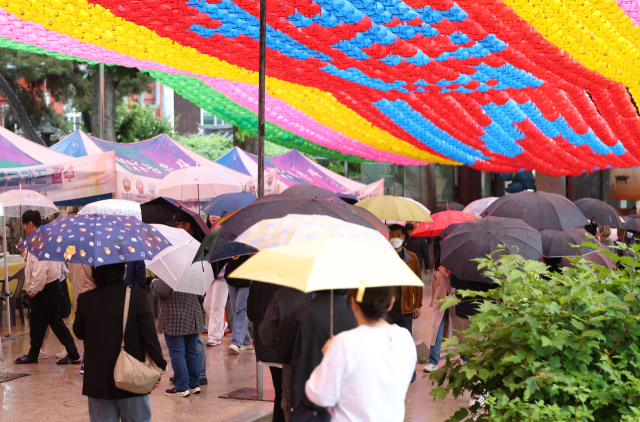 부처님오신날인 15일 오후 서울 강남구 봉은사에 비가 내리자 시민들이 우산을 쓰고 비를 피하고 있다.연합뉴스