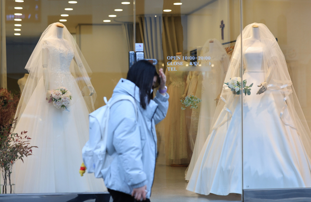 지난해 12월 11일 한 시민이 서울 마포구 아현동 웨딩거리 한 웨딩드레스 판매점 앞을 시민들이 지나가고 있다. 연합뉴스