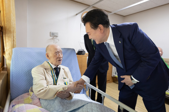 윤석열 대통령이 21일 경기도 수원보훈요양원을 방문해 ‘영웅의 제복’ 재킷을 입고 병상에 앉은 6·25 참전 국가유공자와 인사하고 있다. 연합뉴스