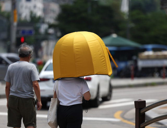 불볕더위가 이어진 21일 서울시내에서 한 시민이 우산을 쓰고 이동하고 있다. 연합뉴스