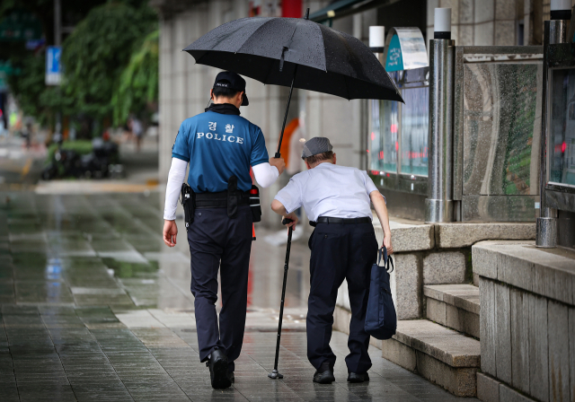 지난달 7일 오전 비가 내리는 서울 종로구 광화문역 인근에서 경찰관이 한 어르신에게 우산을 씌어주고 있다. 뉴스1