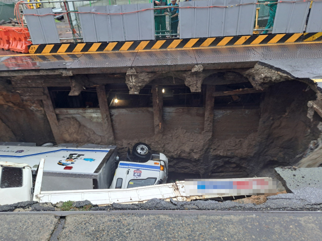 지난 21일 부산 사상구 한 도로에서 대형 싱크홀이 발생해 트럭 2대가 빠져있는 모습. 연합뉴스