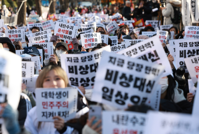 7일 오후 서울 영등포구 여의도 산업은행 본점 인근에서 열린 '윤석열 퇴진 대학생 시국대회'에서 대학생들이 비상계엄을 선포한 대통령의 퇴진을 촉구하며 손팻말을 흔들고 있다.연합뉴스