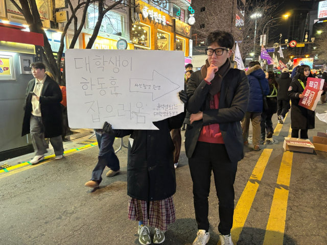 13일 한 대학생이 ‘대학생이 한동훈 잡으러옴’이라고 쓰여 있는 피켓 옆에서 익살스러운 표정을 짓고 있다. 정다은 기자