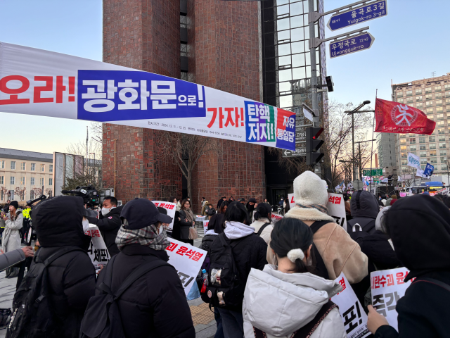 15일 ‘윤석열 체포 김건희 구속 촛불대행진’에 참가한 시민들의 행진 행렬 옆에 자유통일당의 ‘탄핵 저지’ 플랜카드가 걸려 있다. 장형임 기자