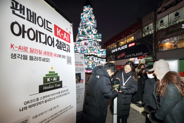 고객들이 서울 신촌 거리에 설치된 KT ‘팬메이드 K-AI아이디어 챌린지’ 팝업 미디어 트리 앞에서 기념 촬영을 하고 있는 모습. 사진 제공=KT