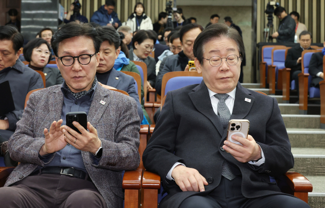 더불어민주당 이재명 대표(오른쪽)와 김민석 의원이 19일 국회에서 열린 비상의원총회에 입장해 휴대폰을 살펴보고 있다. 연합뉴스