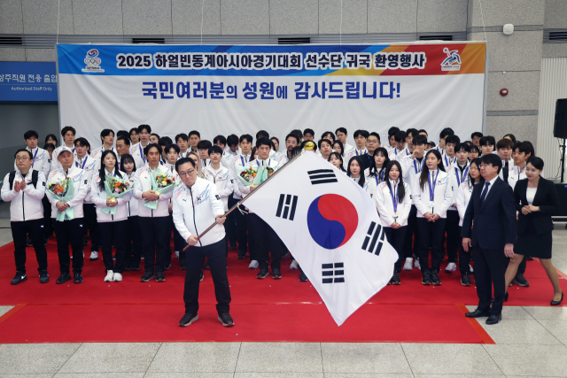 최홍훈 하얼빈 동계아시안게임 선수단장이 15일 인천공항 제1터미널에서 열린 2025 하얼빈 동계아시안게임 귀국 환영행사에서 윤성욱 대한체육회 사무총장에게 단기를 반납하기 전 흔들고 있다. 연합뉴스