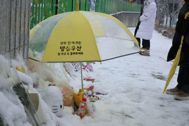 대전 초등학생 김하늘 양 피살사건이 발생한 대전 서구의 한 초등학교 정문에서 12일 오전 학교 관계자가 추모객들이 놓고 간 꽃과 편지 위에 우산을 씌워주고 있다. 연합뉴스