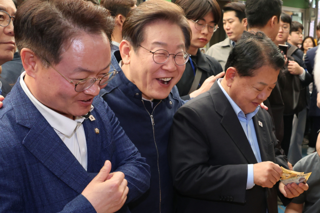 이재명 더불어민주당 대선 후보가 '골목골목 경청투어' 접경지역 방문 이틀째인 2일 강원도 인제군 원통전통시장에서 건어물 가게에 들러 황태채를 맛본 뒤 김병주(오른쪽)·허영 의원에게 구입을 권하고 있다. 연합뉴스
