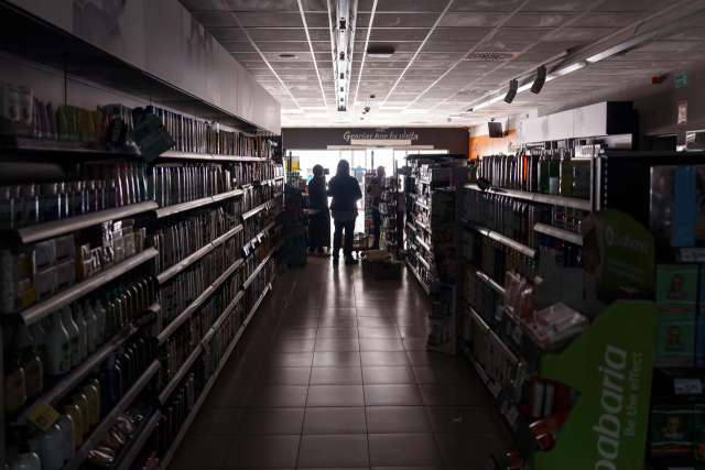 TOPSHOT - Employees stand inside a supermarket without lights in Burgos on April 28, 2025, during a massive power cut affecting the entire Iberian peninsula and the south of France. A \