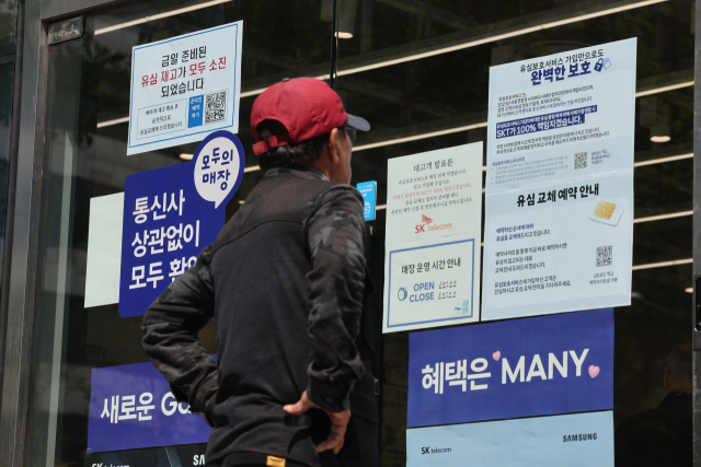 지난 2일 서울 시내의 한 SK텔레콤 대리점 앞에서 한 소비자가 유심 재고 소진 및 유심보호서비스 관련 안내문을 살펴보고 있다. 연합뉴스