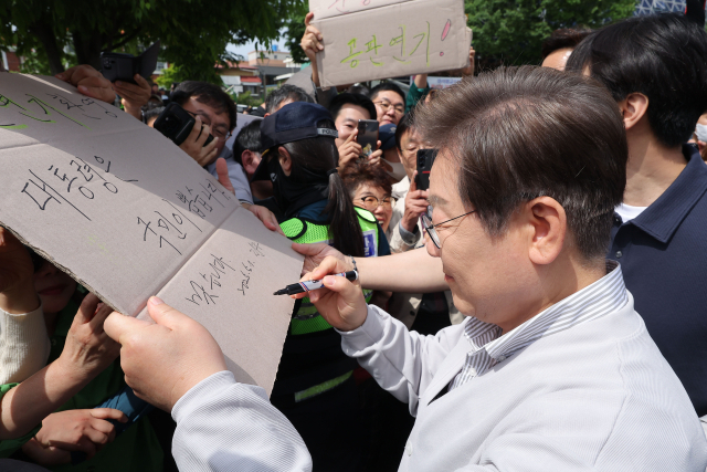 이재명 더불어민주당 대선 후보가 '골목골목 경청투어:국토종주편'에 나선 7일 전북 전주시 풍남문 앞 광장에서 지지자들에게 인사를 하던 도중 한 지지자가 든 '공판 연기 환영, 대통령은 국민이 뽑습니다'라는 팻말에 사인을 하고 있다. 이날 서울고등법원은 오는 15일 예정됐던 이 후보의 공직선거법 위반 혐의 사건 파기환송심 첫 공판을 오는 6월 18일로 연기했다. 연합뉴스