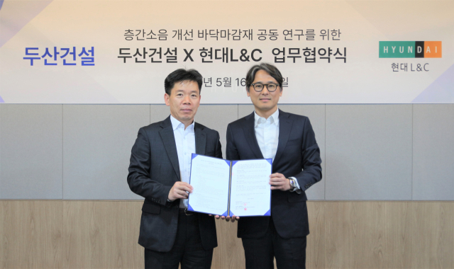 신홍철 두산건설 상무가 16일 서울 강동구 현대L&C 본사에서 성재용 상무를 만나 층간소음 개선을 위한 바닥 마감재 공동 연구 업무협약을 체결한 후 기념사진을 찍고 있다. 사진 제공=두산건설