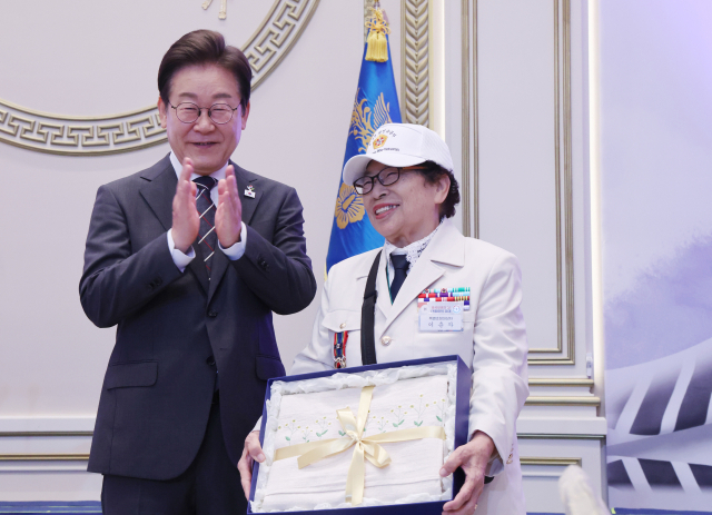 이재명 대통령이 27일 청와대 영빈관에서 열린 ‘호국 보훈의 달, 대통령의 초대’ 행사에서 특별 초청대상자인 이춘자 씨에게 광목 이불을 선물한 뒤 박수치고 있다. 연합뉴스