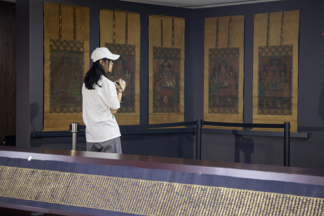 8일 ‘고려 사경과 조선 불화의 귀환' 행사에서 한 참석자가 감지금니 대방광불화엄경 주본 권22(아래쪽)와 시왕도를 살펴보고 있다. 연합뉴스