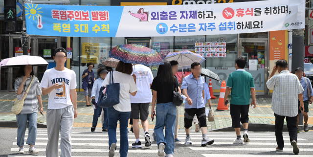 서울 전역에 폭염경보가 발령되는 등 가마솥더위가 이어진 24일 양산을 쓴 시민들이 서울 서대문구 거리에서 폭염시 행동 수칙이 담긴 현수막 앞을 지나고 있다. 금요일인 25일과 토요일인 26일에는 서울의 한낮 최고기온이 각각 37도와 38도까지 오를 것으로 보인다. 오승현 기자