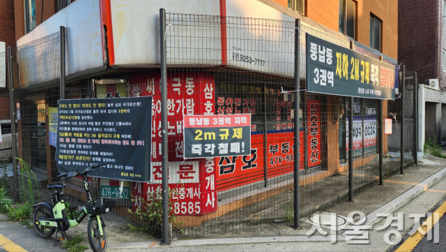 ‘규제 때문에 못살겠다’는 플래카드들이 붙어 있다. 정비 대상인 건물이 철제 울타리에 둘러싸여 있다.