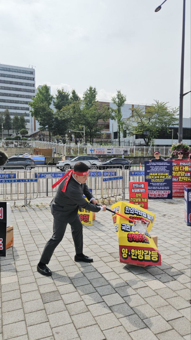 임채윤 대한한약사회장이 29일 대통령집무실앞 집회에서 불합리한 현실이 적힌 피켓을 격파하는 퍼포먼스를 벌이고 있다. 사진 제공=대한한약사회